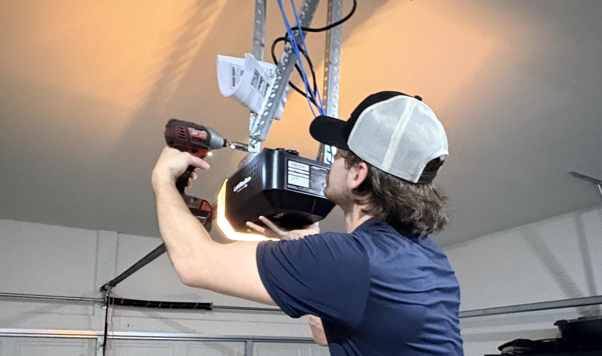 Technician with a drill tightening a bolt for the garage door operator.